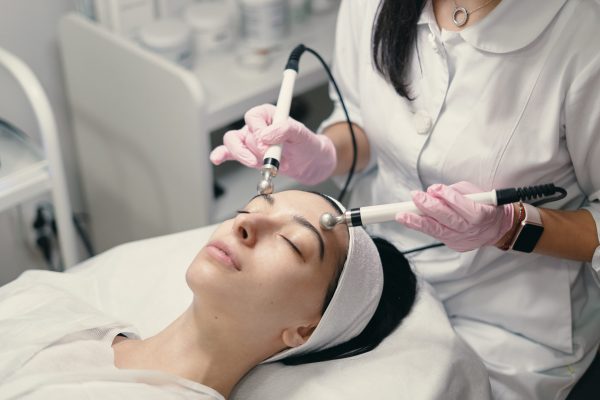 Model with closed eyes and hand's of doctor. Rejuvenating facial treatment. Model getting lifting therapy massage in a beauty SPA salon. Cosmetological clinic, procedure.